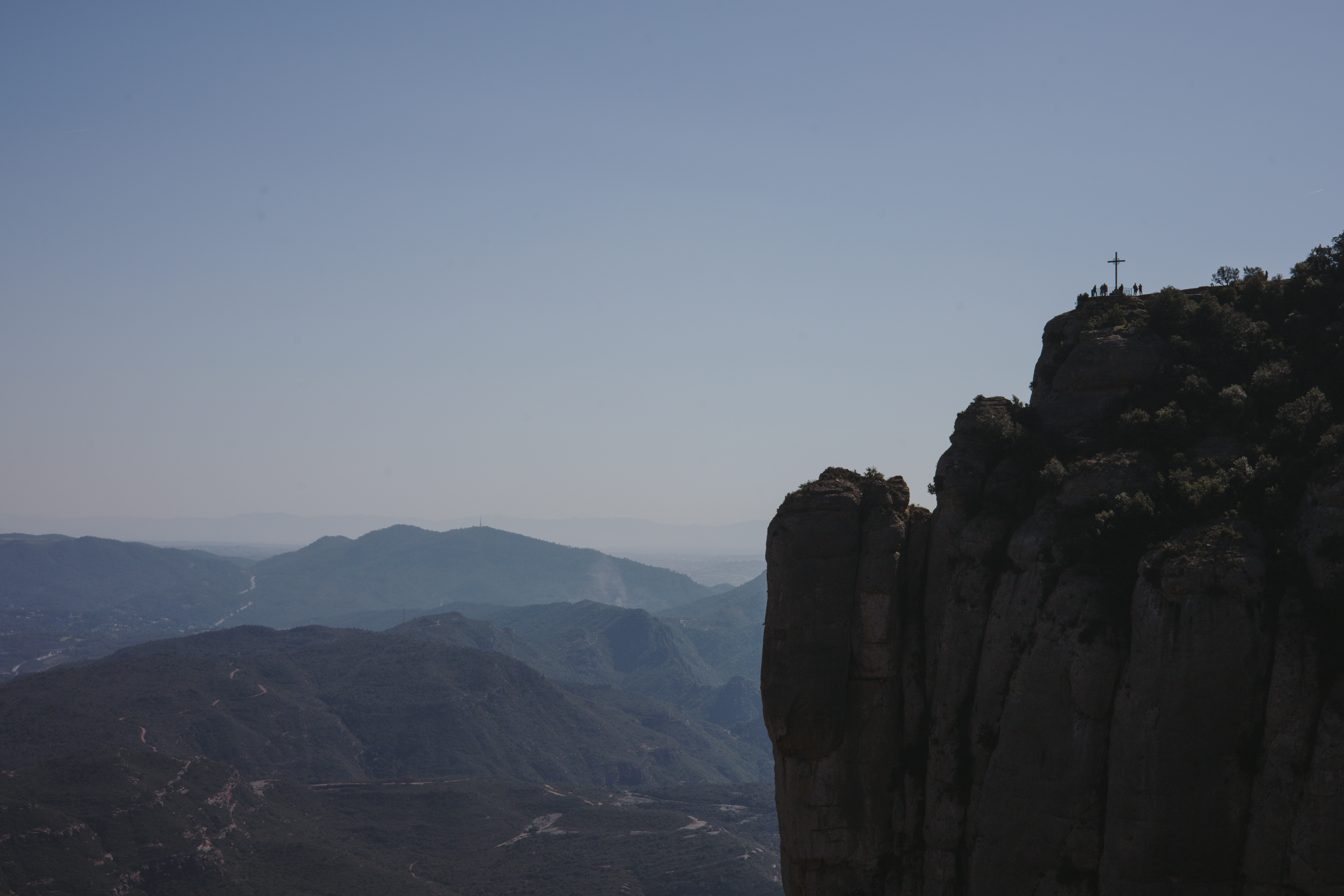 Acantilado de Montserrat con la cruz de Sant Miquel en la cima, con el paisaje verde a los pies de la montaña.