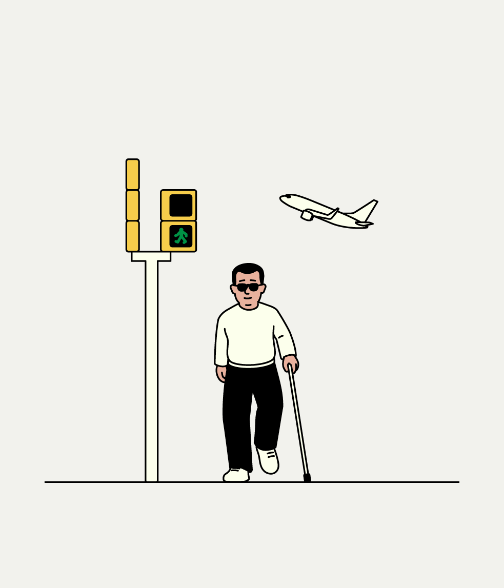 Persona amb bastó blanc travessant un pas de vianants amb semàfor sonor mentre un avió sobrevola la ciutat.