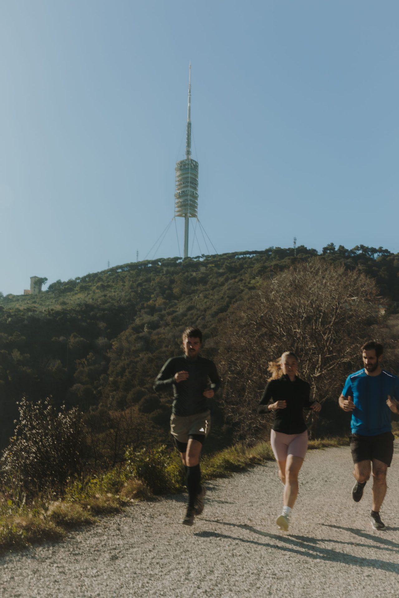 Tres persones corrent per un camí de terra en una zona natural, amb la Torre de Collserola al fons.