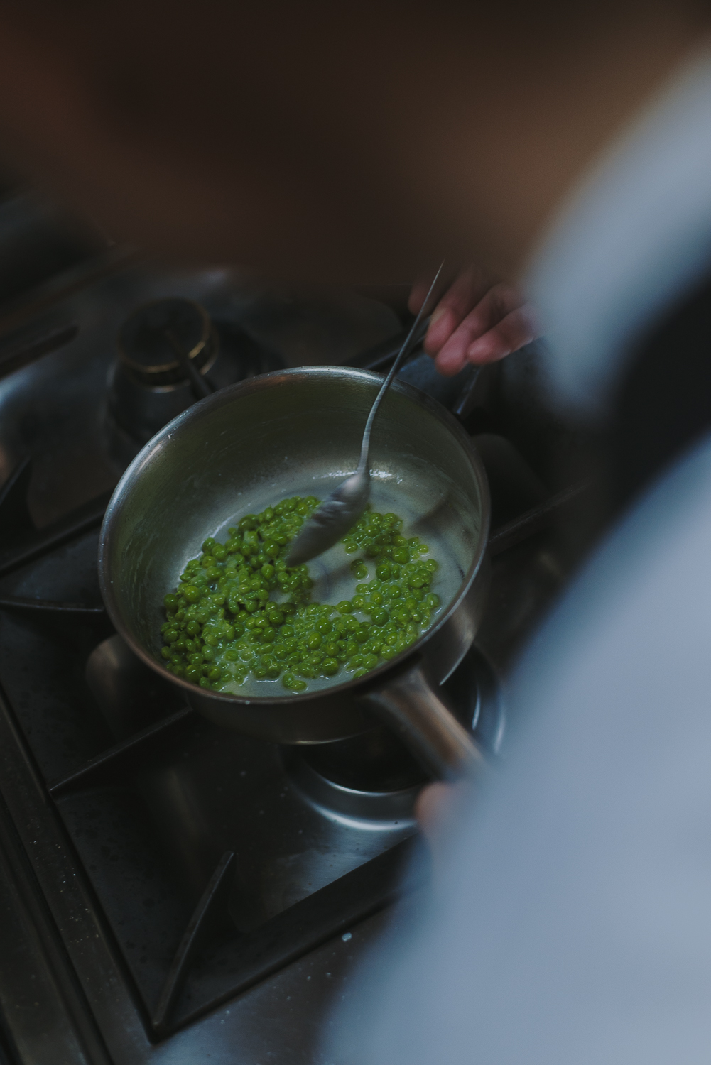  Cazo con guisantes verdes cocinándose al fuego mientras una persona los remueve con una cuchara en una cocina profesional.