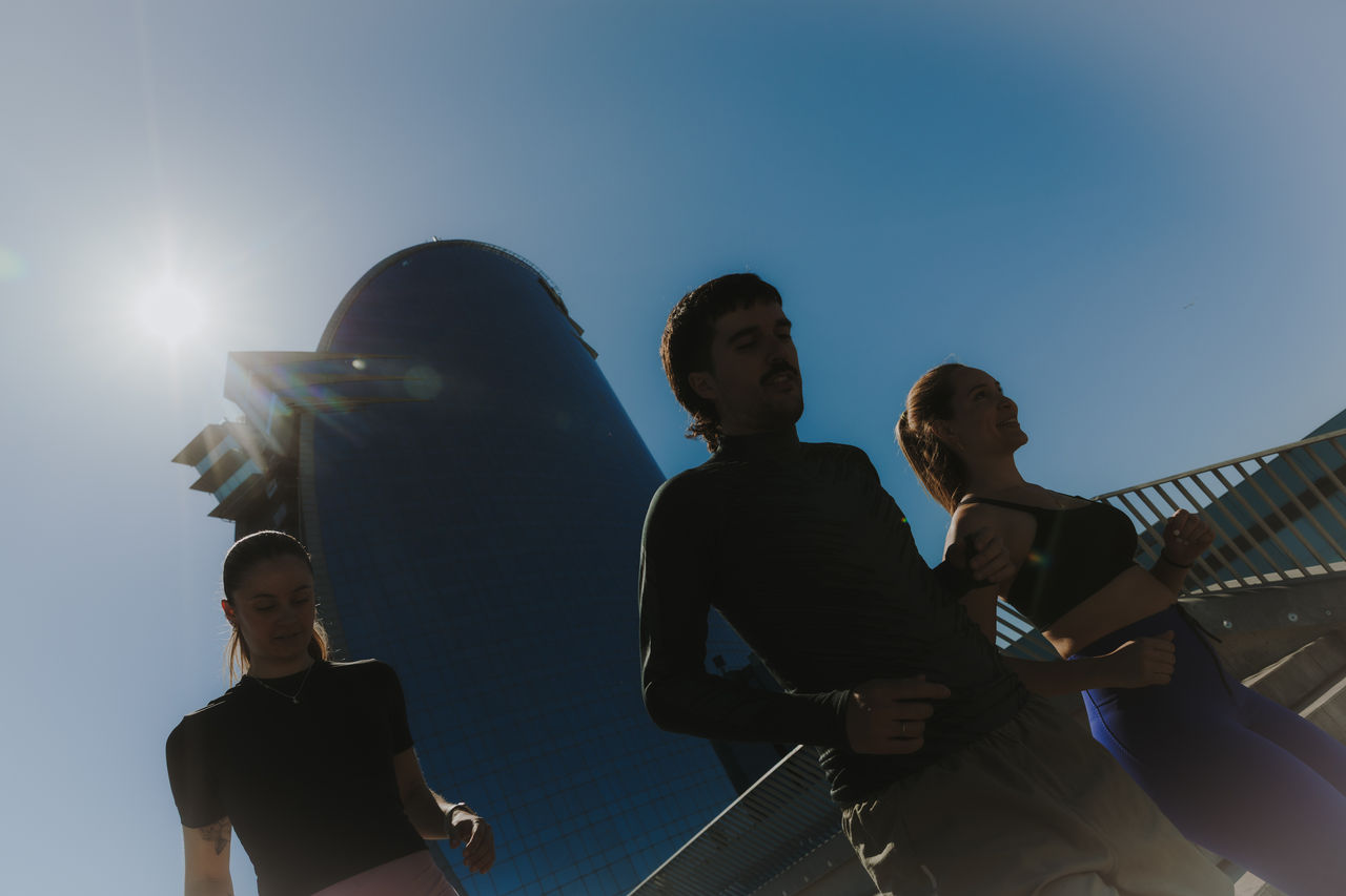 Trois personnes courent avec l’hôtel W Barcelona à l’arrière-plan, sous un ciel bleu et à contre-jour.