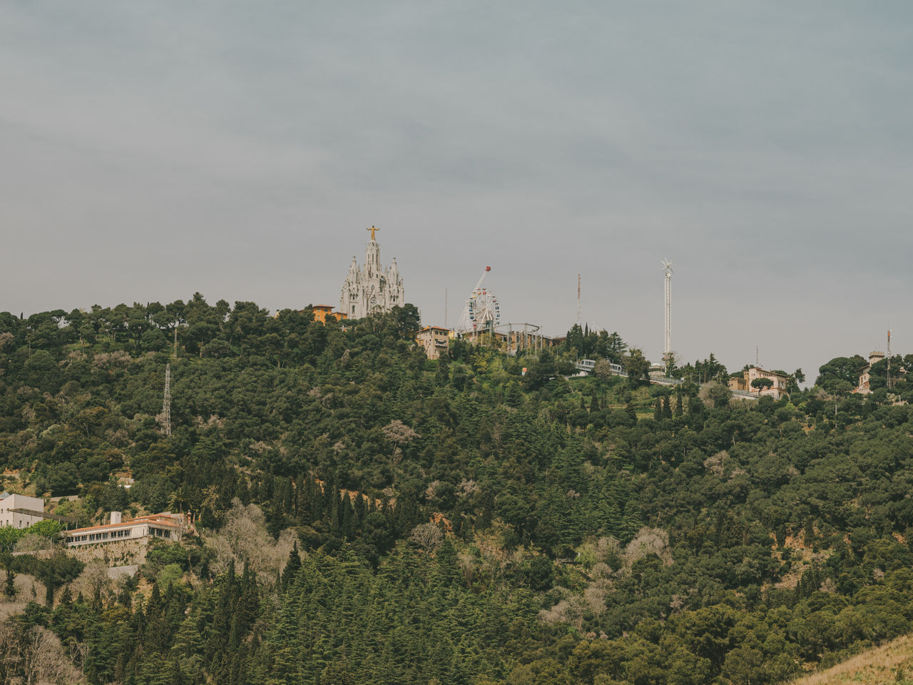 Vista della montagna del Tibidabo con il Temple Expiatori del Sagrat Cor, il parco divertimenti e abbondante vegetazione circostante.