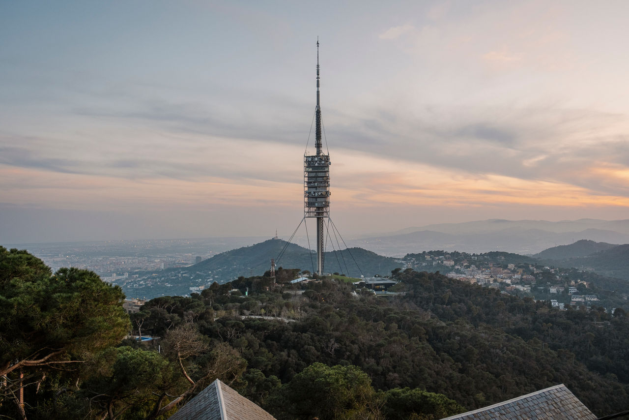 Vista del Tibidabo con la Torre di Collserola al centro, circondata dal bosco e con la città di Barcellona sullo sfondo al tramonto